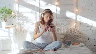 戴着耳机听着智能<strong>手机音乐</strong>在床上跳舞的快乐女人